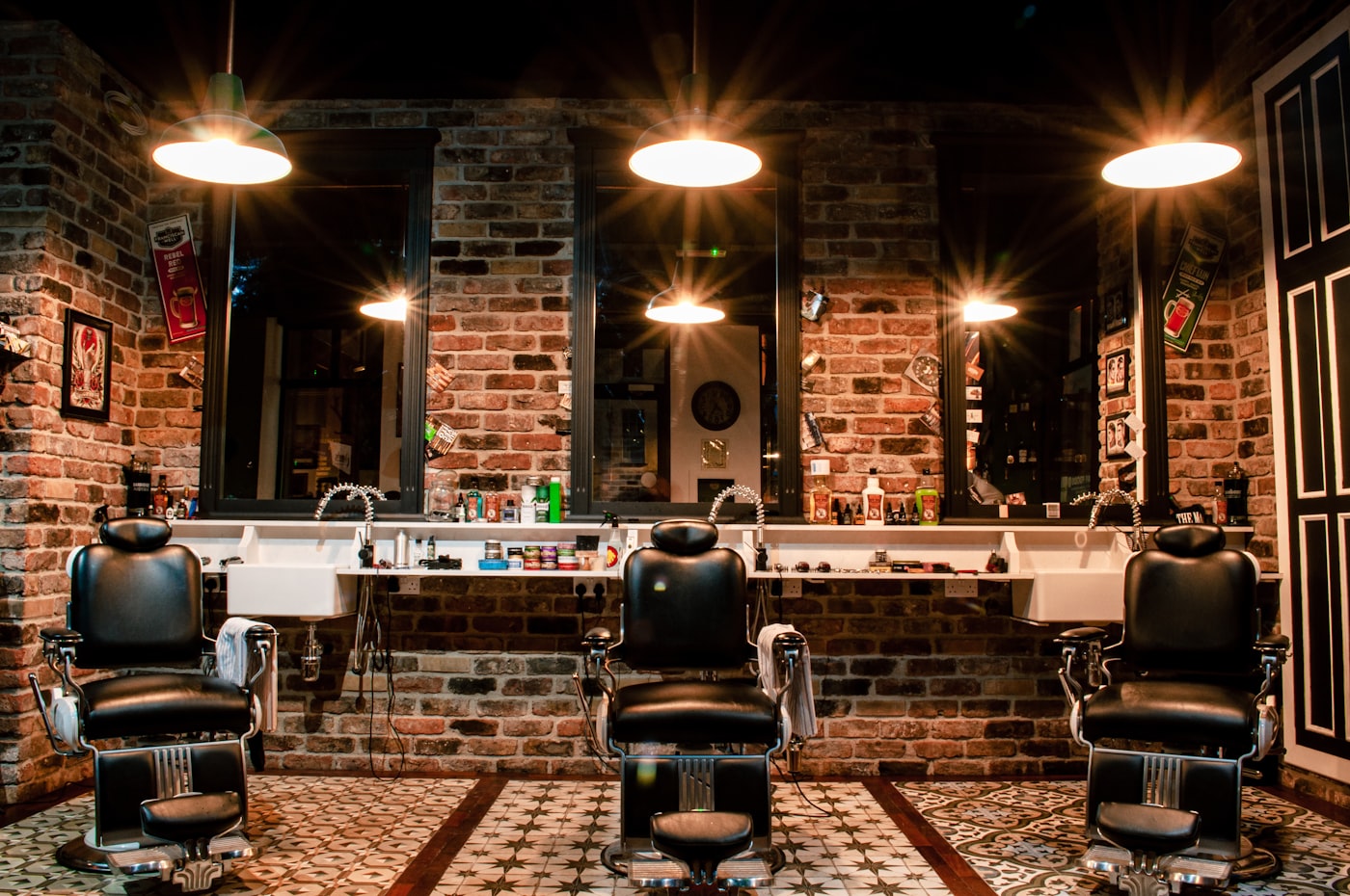 Warm-lit barbershop chairs against a brick wall