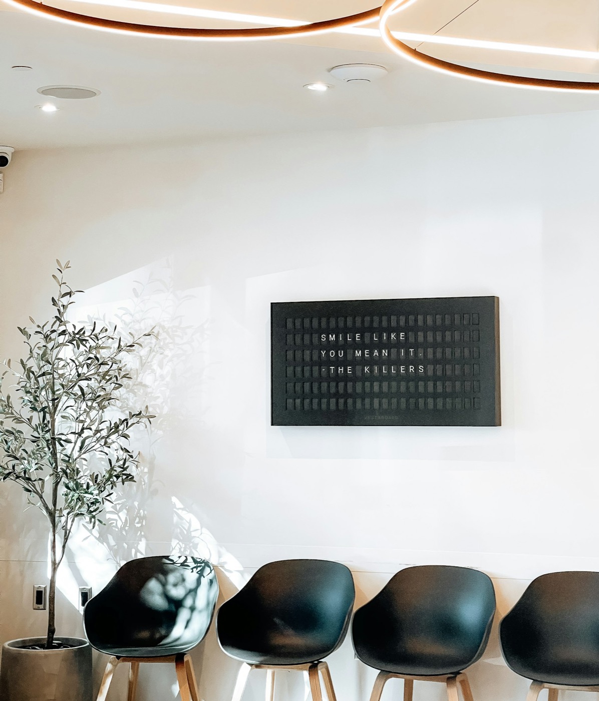 Calm, light-filled dental waiting room with a warm letterboard sign reading 'smile like you mean it'