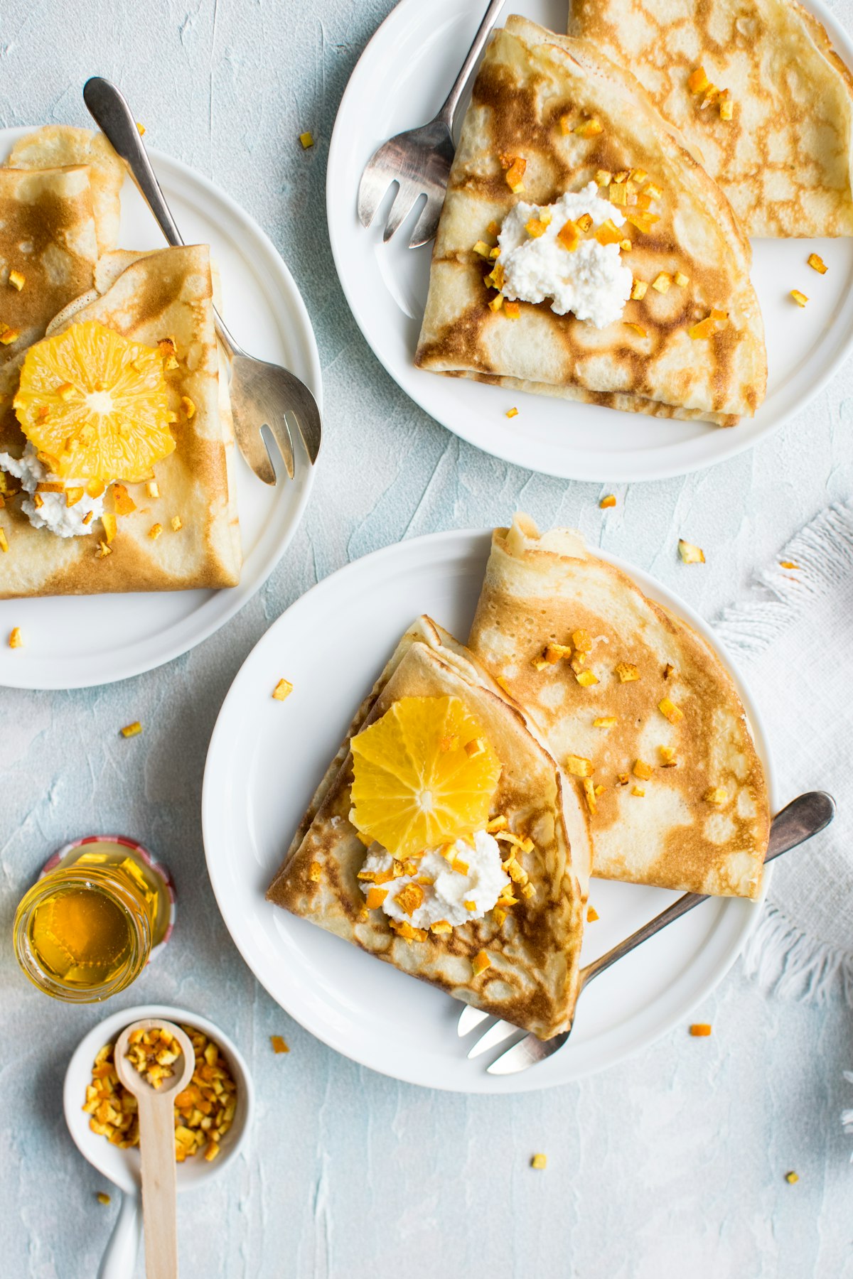 Folded crêpes with citrus and cream on white plates