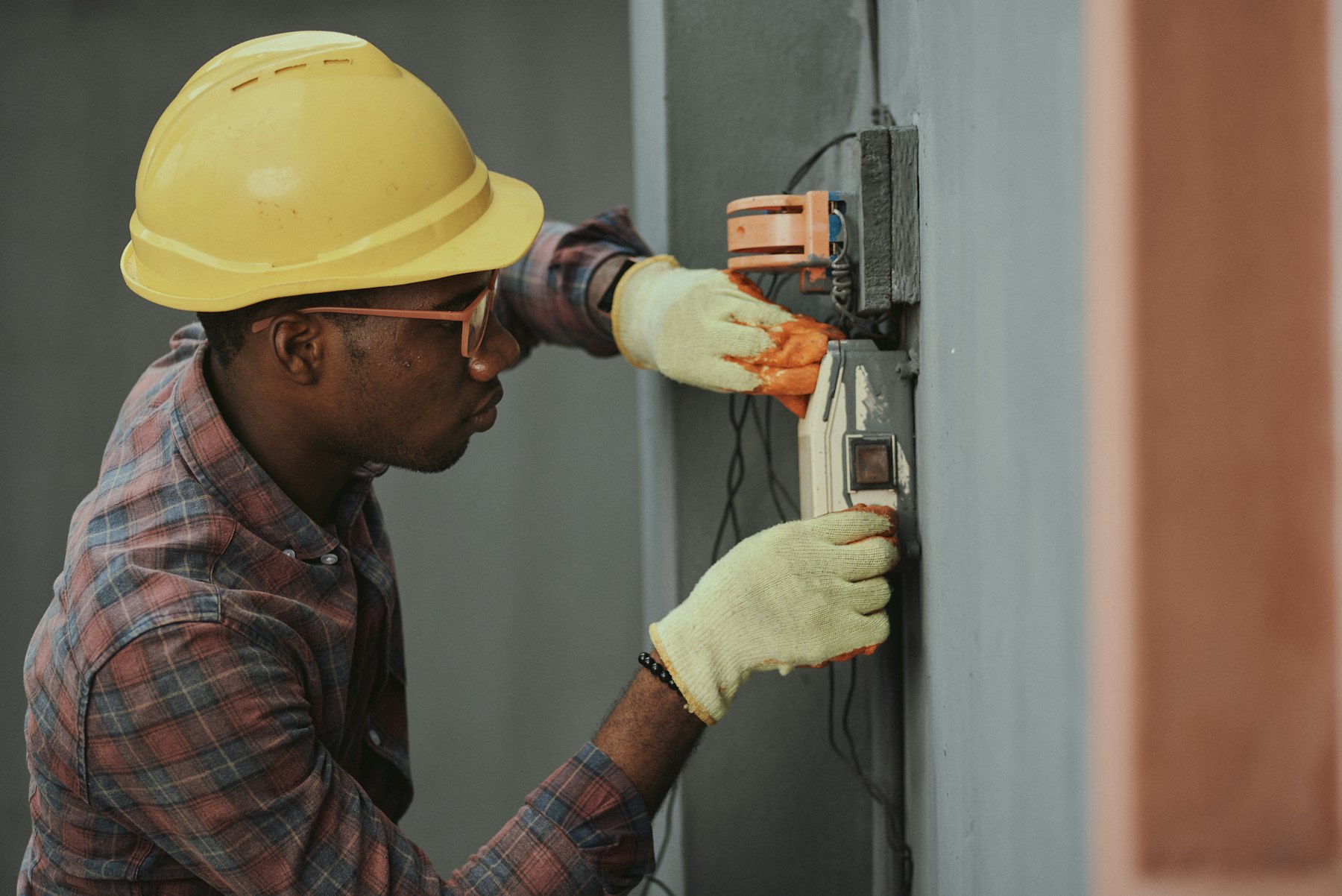 Electrician in hard hat wiring a switch unit on site