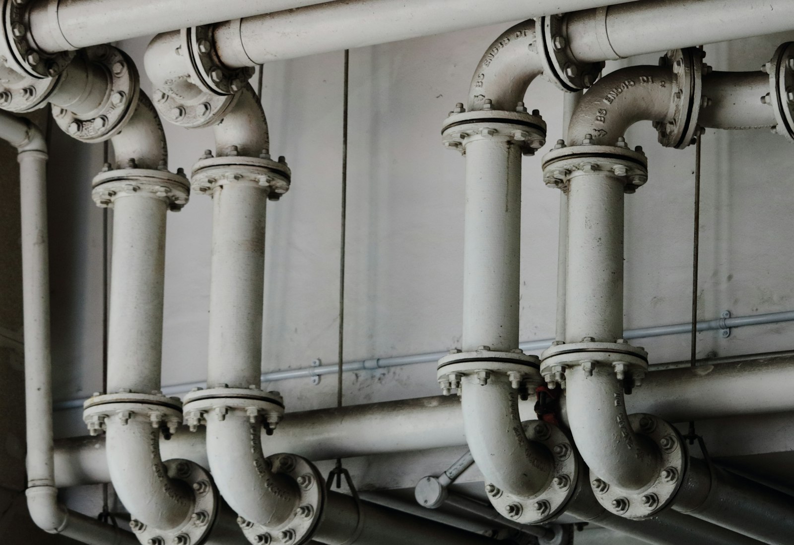 Dense run of steel plumbing mains against a concrete wall