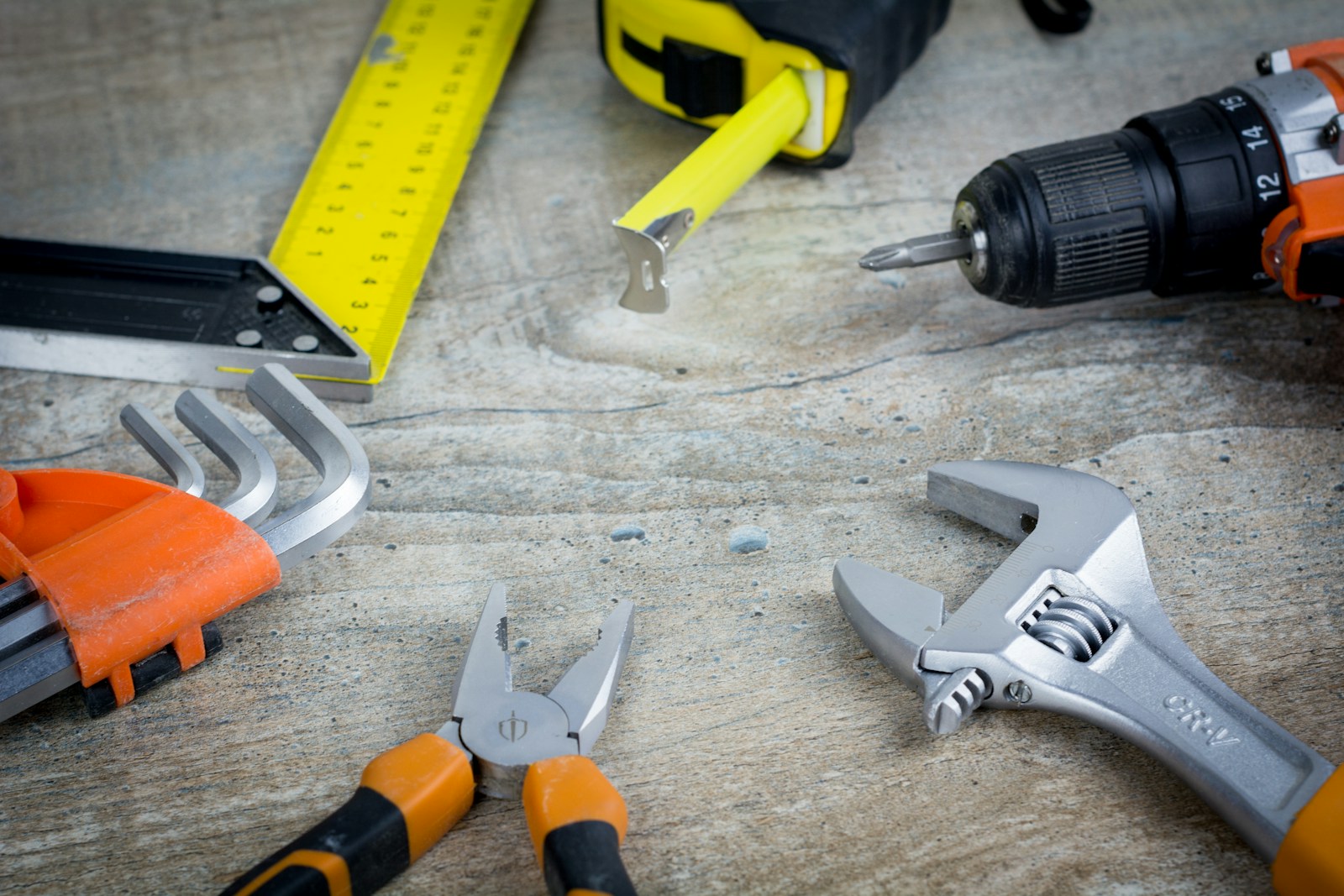 Pliers, wrench, drill and tape measure laid out on a worn wooden bench