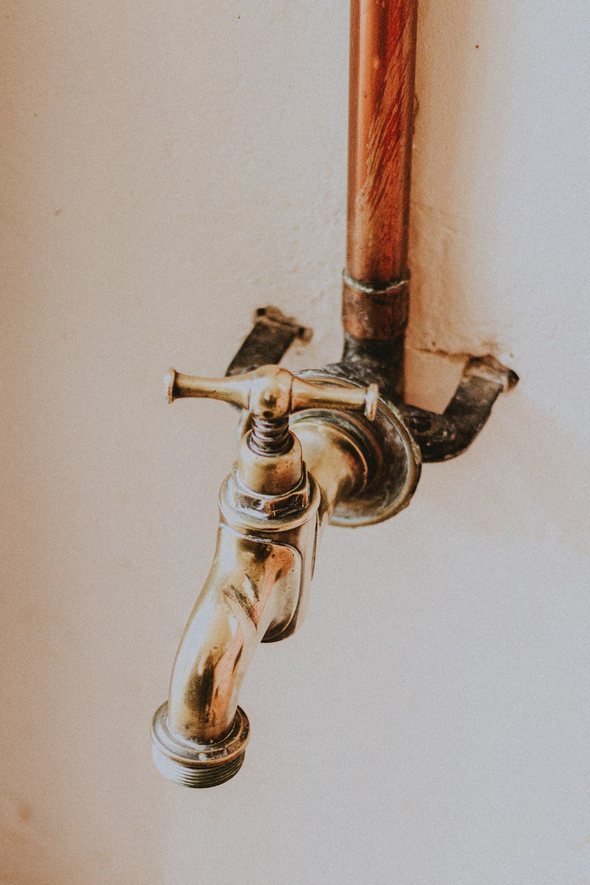Polished brass tap and copper pipe against a porcelain-white wall